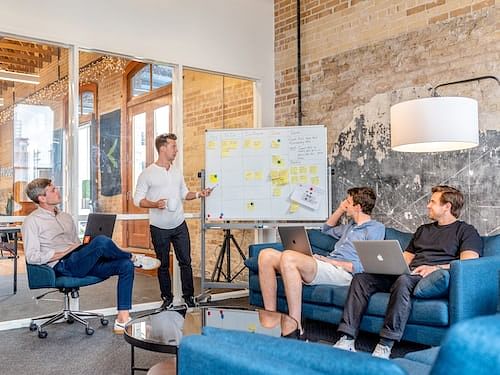 A group of college students brainstorming ideas for their projects, using Chat GPT Prompts on their laptops and tablets, while surrounded by books, papers, and a whiteboard filled with ideas.